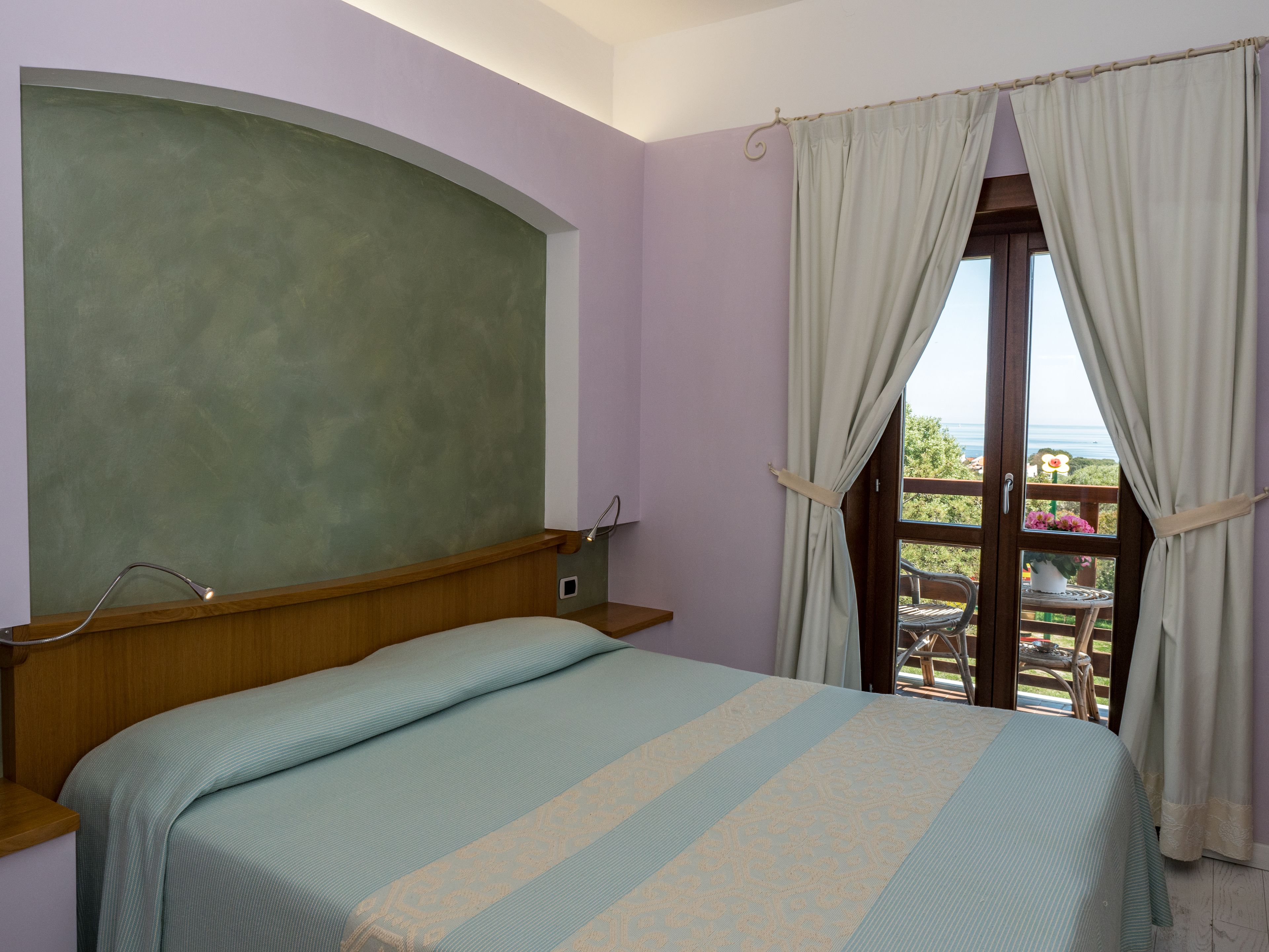 Un dormitorio con cama, cabecera de madera, ventana con cortinas y vistas al exterior.