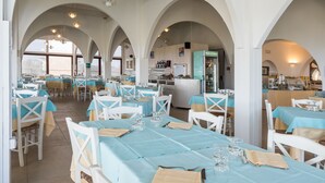 A restaurant with multiple tables, white chairs, and blue tablecloths. - Hotel Cala Reale (Stintino)
