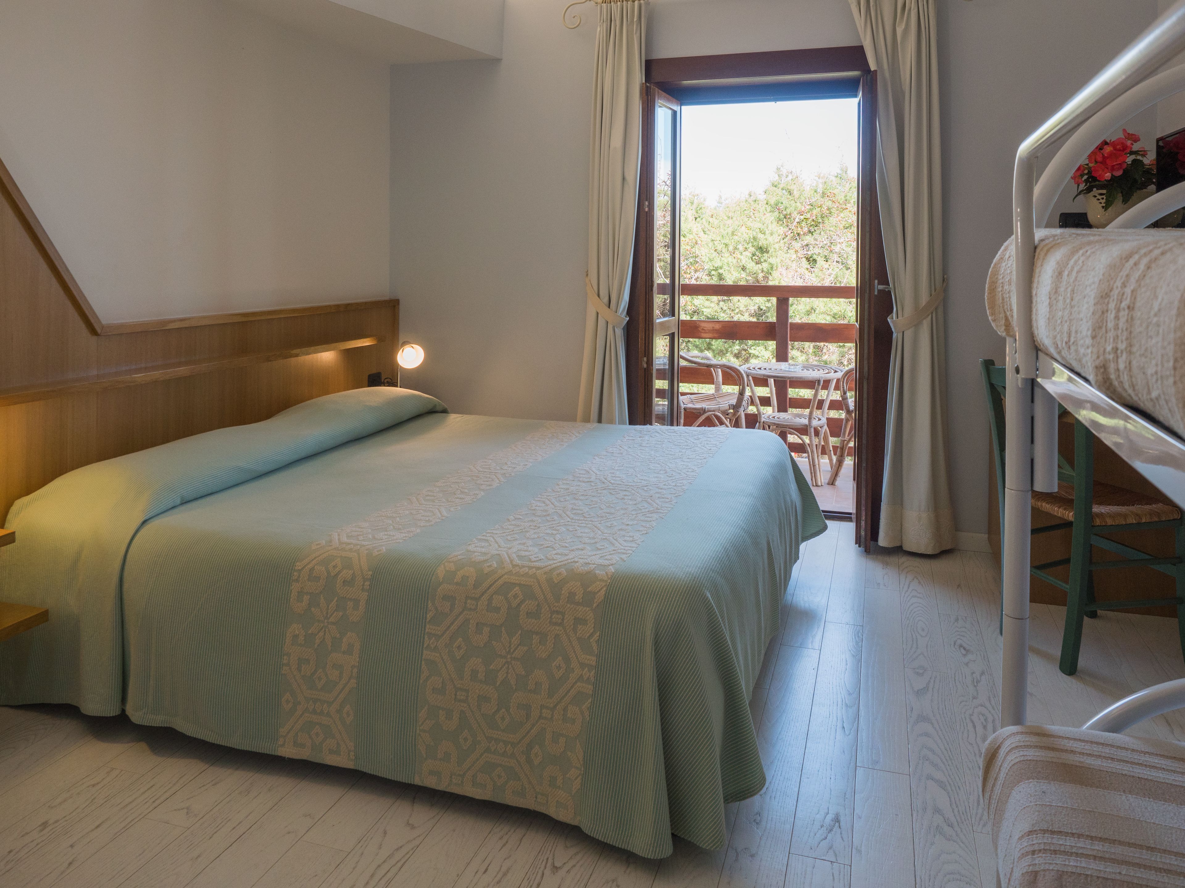 Un dormitorio con cama, mesita de noche, ventana con cortinas y vistas al exterior.