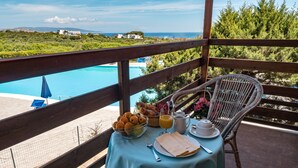 A balcony with a table set for breakfast, overlooking a pool and greenery. - Hotel Cala Reale (Stintino)