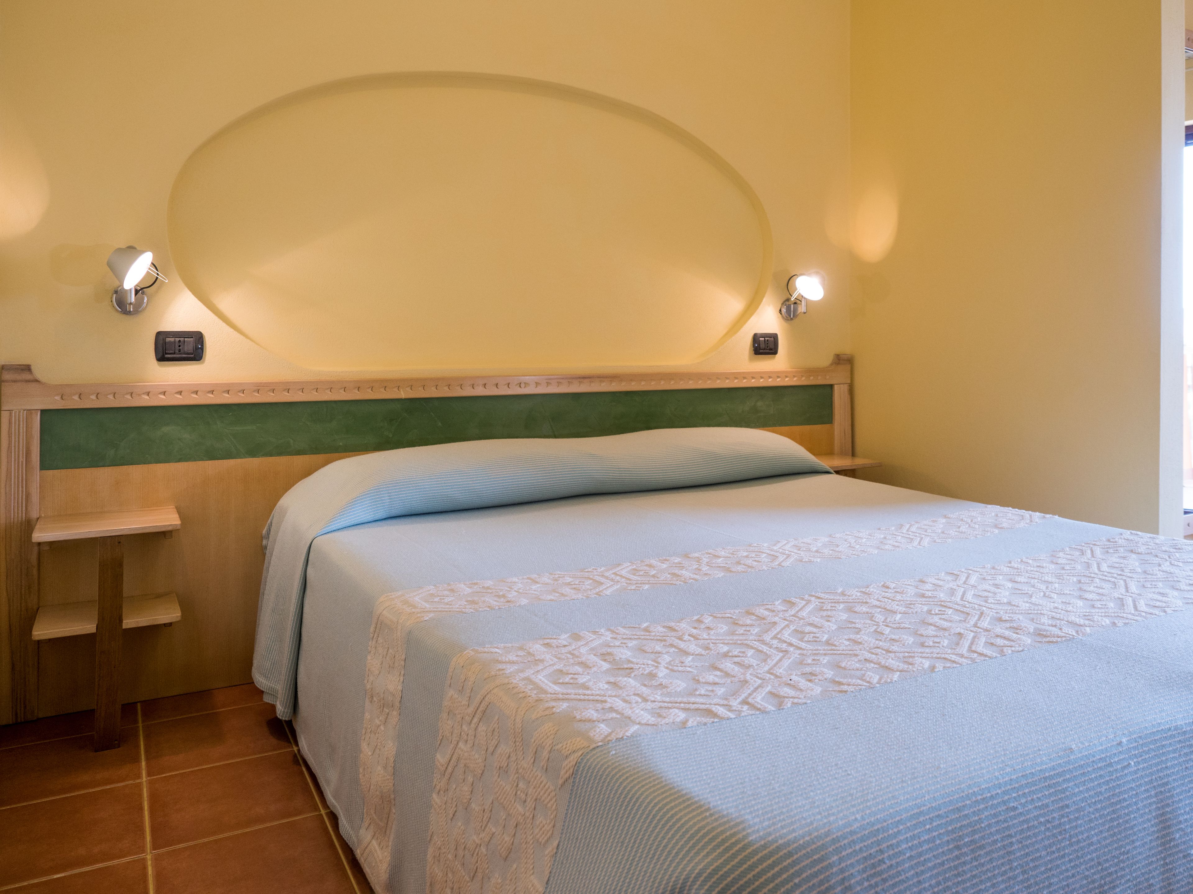 Een hotelkamer met een bed, een nachtkastje, een wandlamp en een stopcontact.
