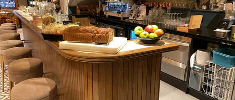 A bar area with a wooden counter, seating, and a bowl of fruit.