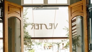 A restaurant interior with wooden furniture, a large window with a view of the street, and a sign with partially visible text. - Amadeus Hotel (Haarlem)