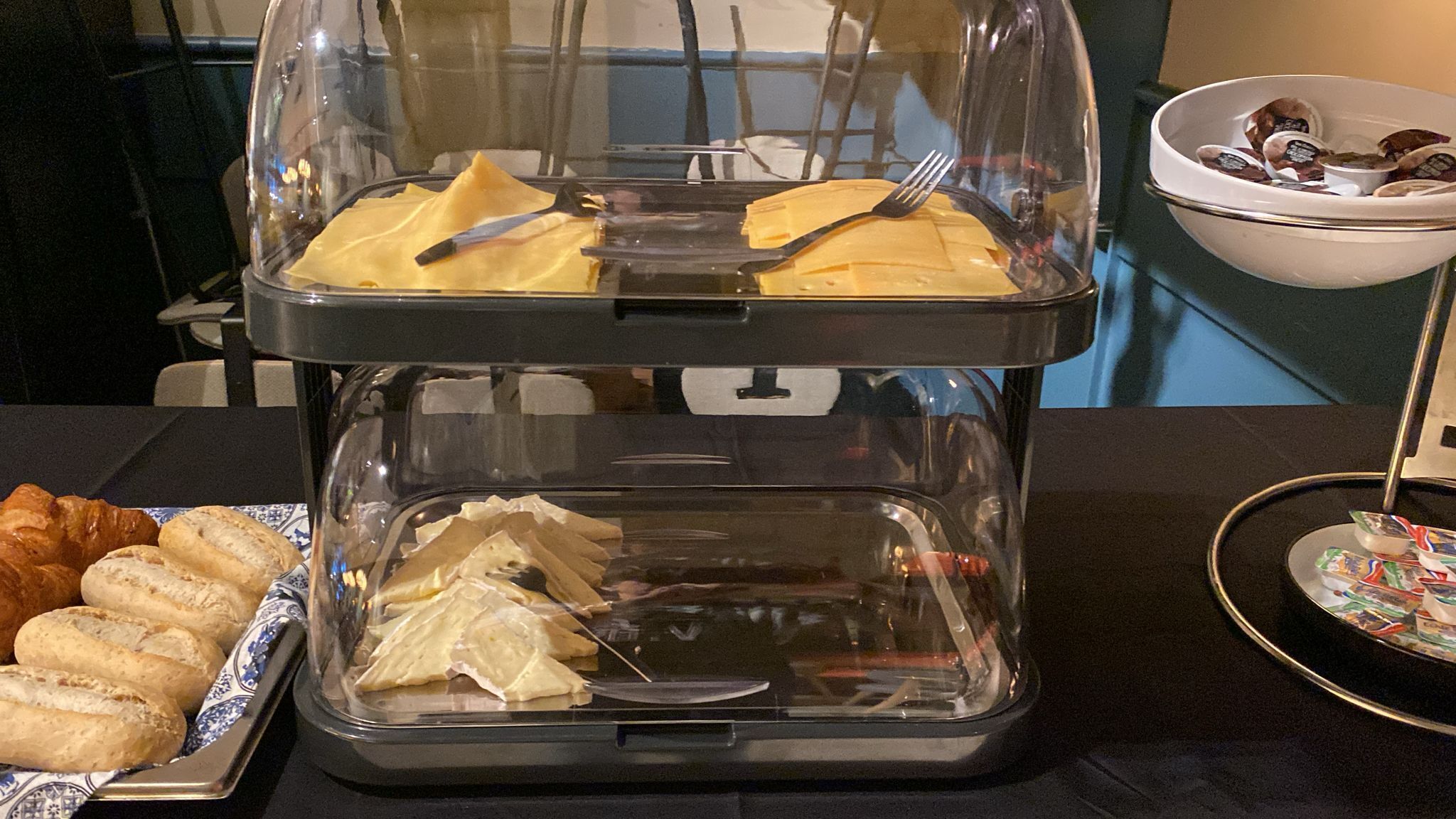 A buffet setup with two glass-covered trays, one with pastries and the other with sandwiches.