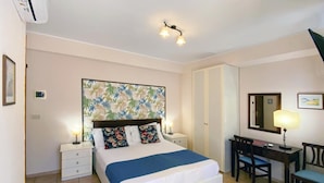 A hotel room with a bed, bedside tables, a desk with a chair, a mirror, and a ceiling light fixture. - Casa Famiani Bed & Breakfast (Letojanni)