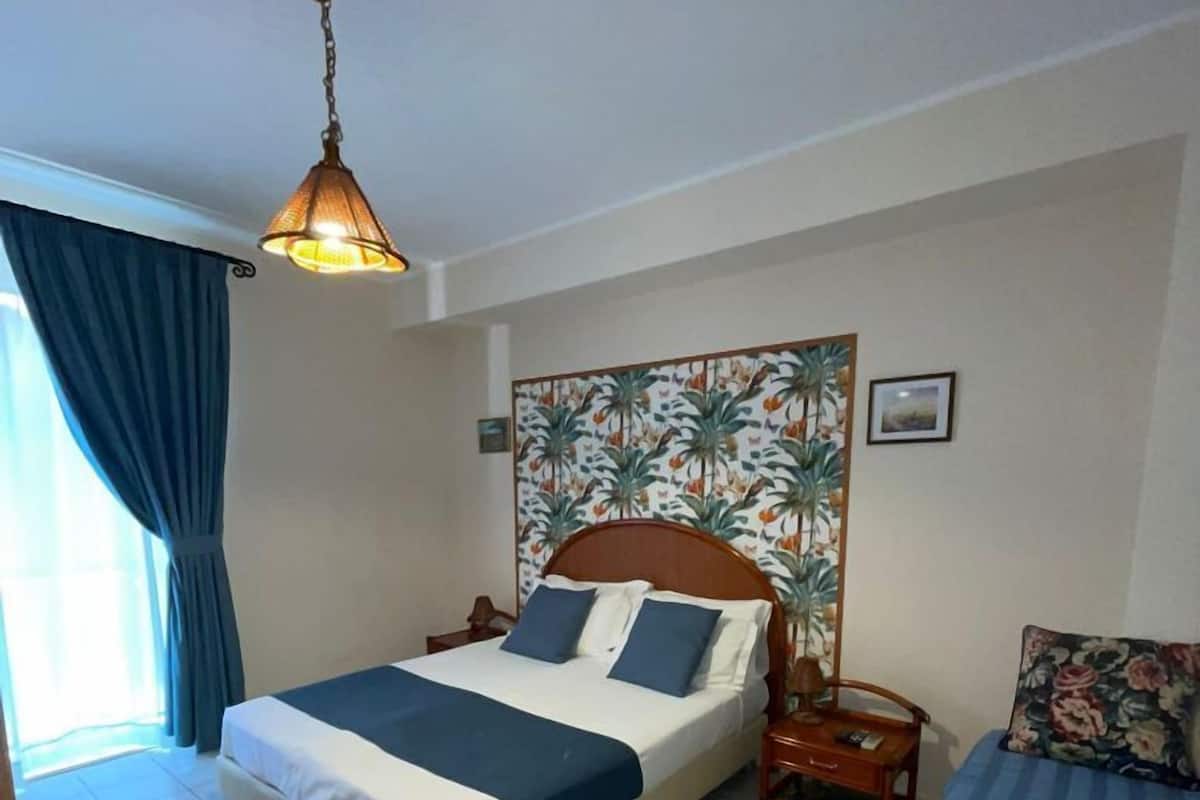 A bedroom with a bed, a nightstand, a lamp, and a painting on the wall.