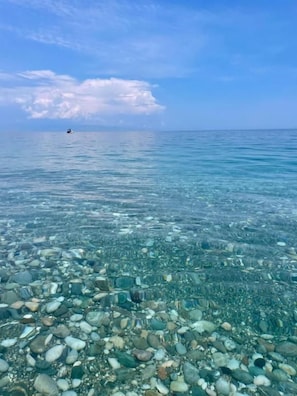 A clear view of a beach with a boat in the distance and a rocky shoreline. - Casa Famiani Bed & Breakfast (Letojanni)