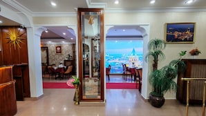 A hotel lobby with a view of a cityscape through a large window. There are dining tables and chairs, a red carpet, and a potted plant. - Sirkeci Emek Hotel (Istanbul)