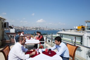 A rooftop dining area with tables set for four, overlooking a cityscape and the sea. - Sirkeci Emek Hotel (Istanbul)