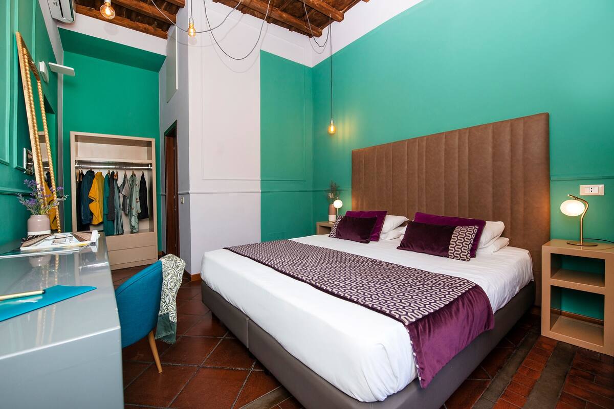 A bedroom with a large bed, a wardrobe, a desk, and a mirror.