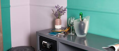 A compact room with teal and white walls, a small table with a vase of flowers, a bottle of champagne, and a few glasses.