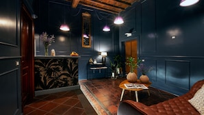 Une pièce aux murs bleu foncé, avec un plafond en bois et un canapé en cuir marron. On y trouve une petite table sur laquelle sont posés une lampe et un vase de fleurs.