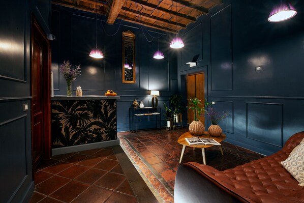 A room with dark blue walls, a wooden ceiling, and a brown leather sofa. There is a small table with a lamp and a vase of flowers.