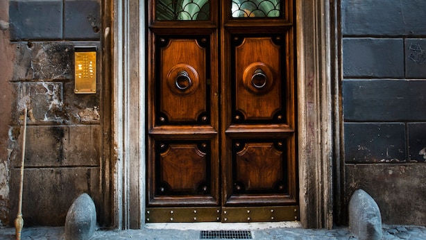 Une porte à deux battants en bois, dotée d’une plaque de protection métallique, intégrée à un bâtiment en pierre dont la façade est en briques.