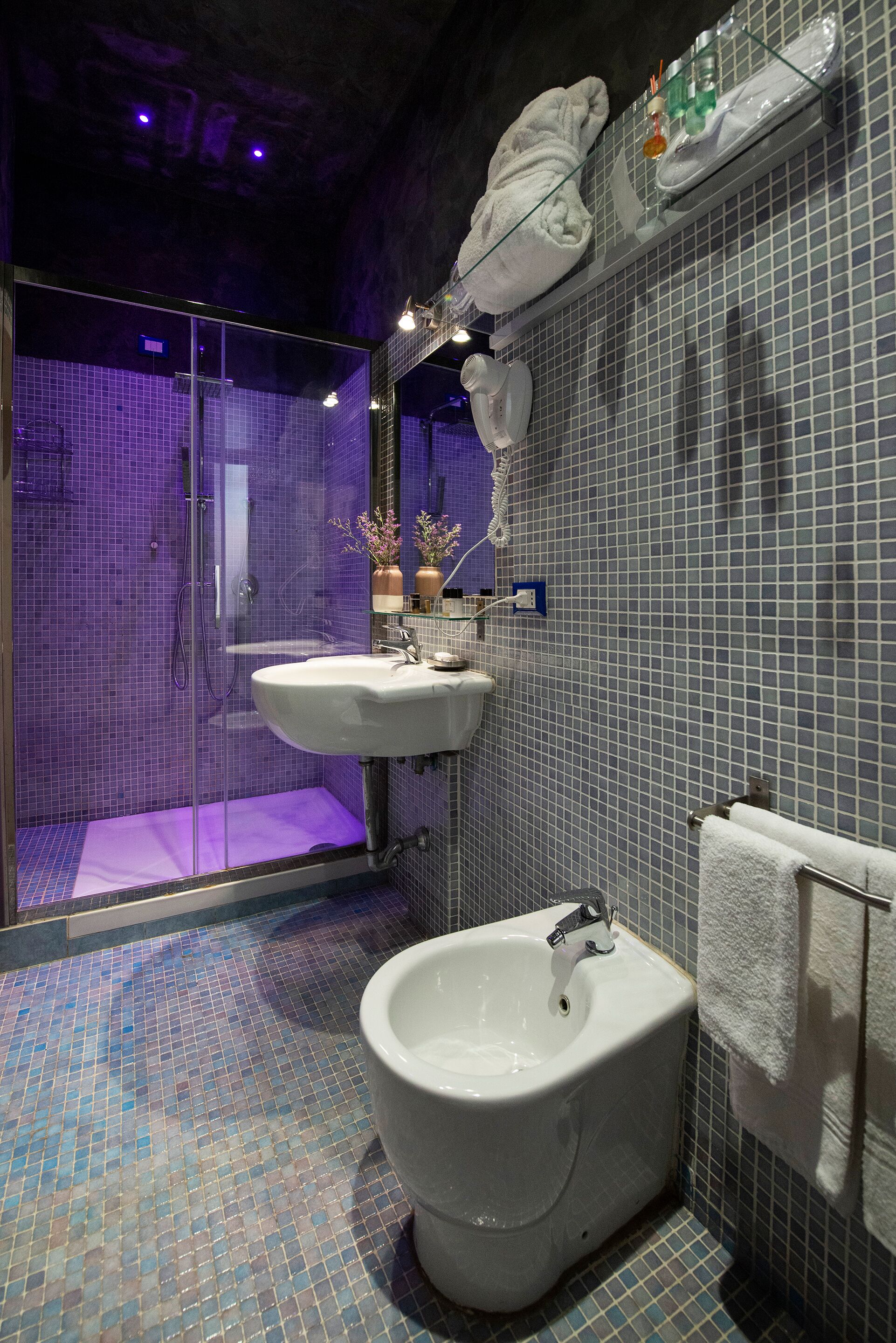A bathroom with a bidet, a glass-enclosed shower, and a tiled floor.