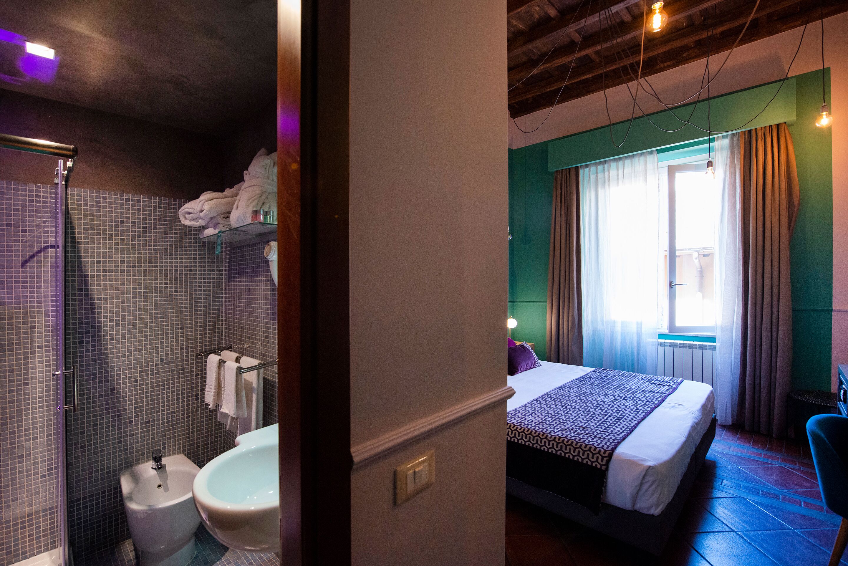 A hotel room with a shower, a sink, a bed, and a window with curtains.
