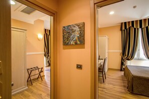A hotel room with a wooden floor, a bed with a patterned bedspread, a desk with a chair, a painting on the wall, and curtains on the window. - PapavistaRelais (Rome)