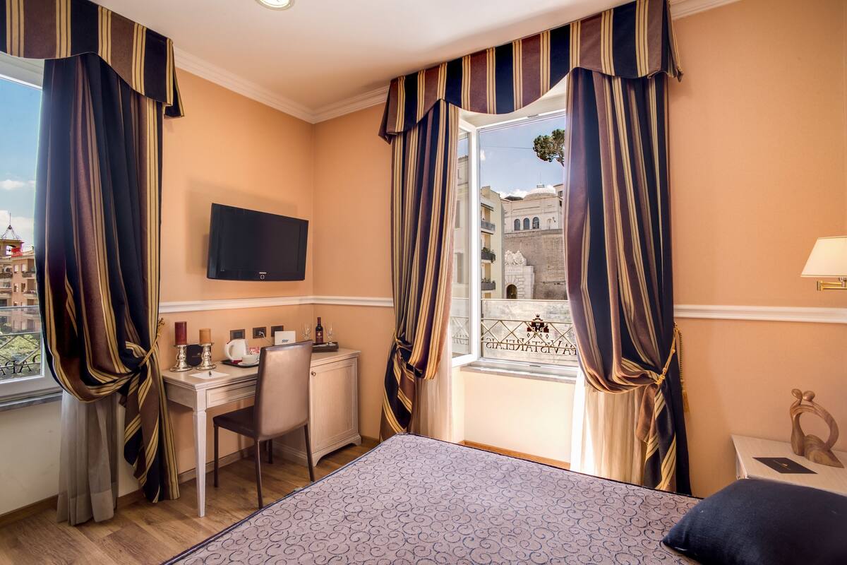 A hotel room with a bed, a desk, a chair, a TV, and a window with curtains.