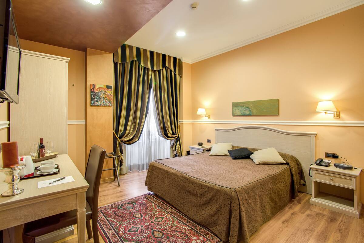A hotel room with a bed, bedside table, lamp, desk, chair, and a rug.