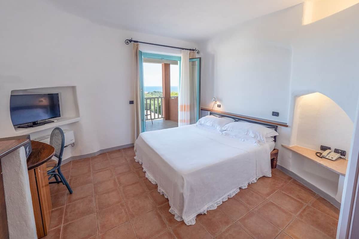 Un dormitorio con cama, televisión, escritorio y balcón.