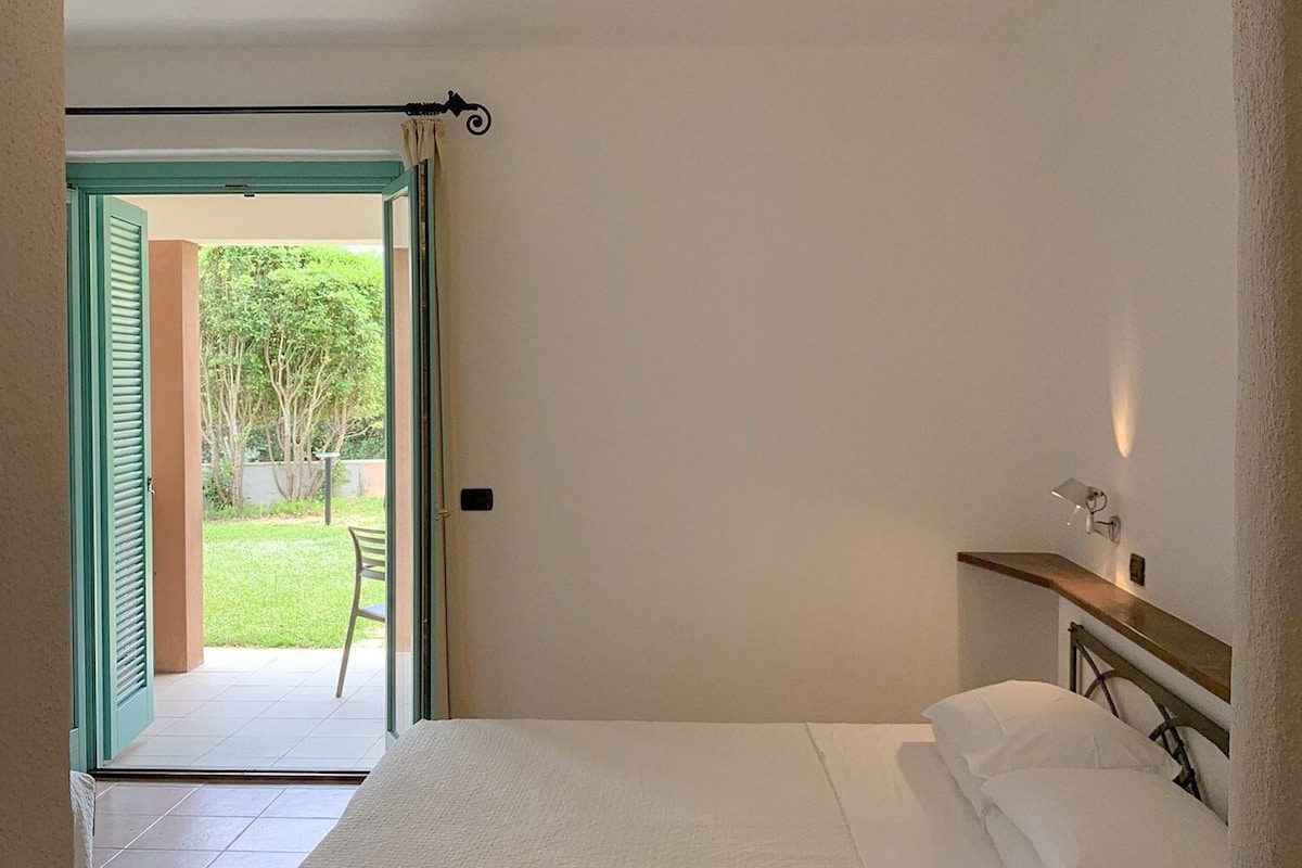Un dormitorio con cama, una mesita de noche y vistas a un jardín por una puerta abierta.