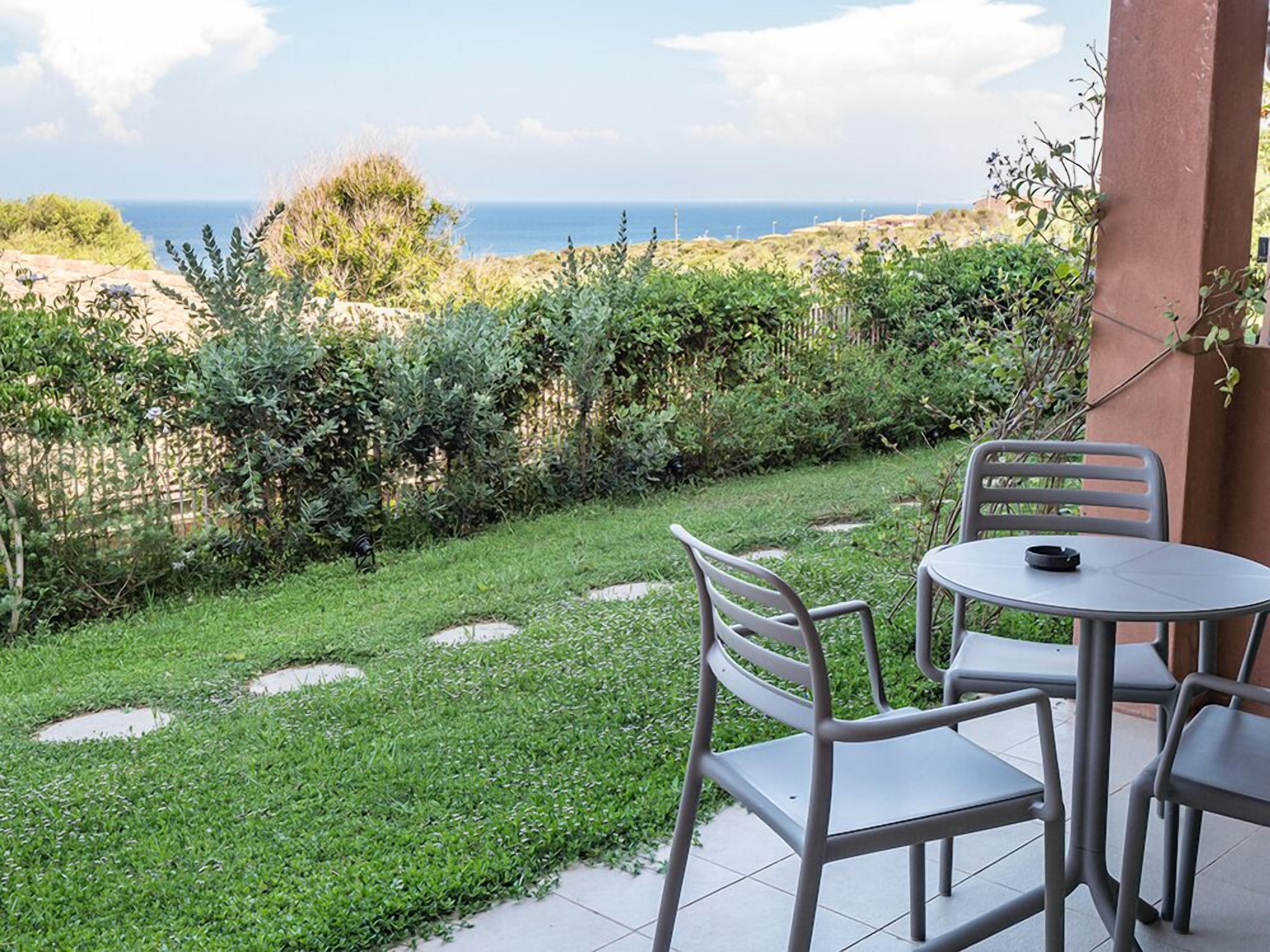 Eine Terrasse mit Tisch und Stühlen mit Blick auf eine Wiese und das Meer.
