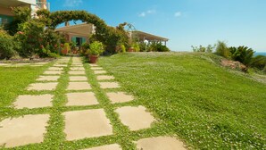 Una casa con un sendero de piedra que conduce a un porche cubierto, rodeada de exuberante vegetación y un cielo azul claro.
