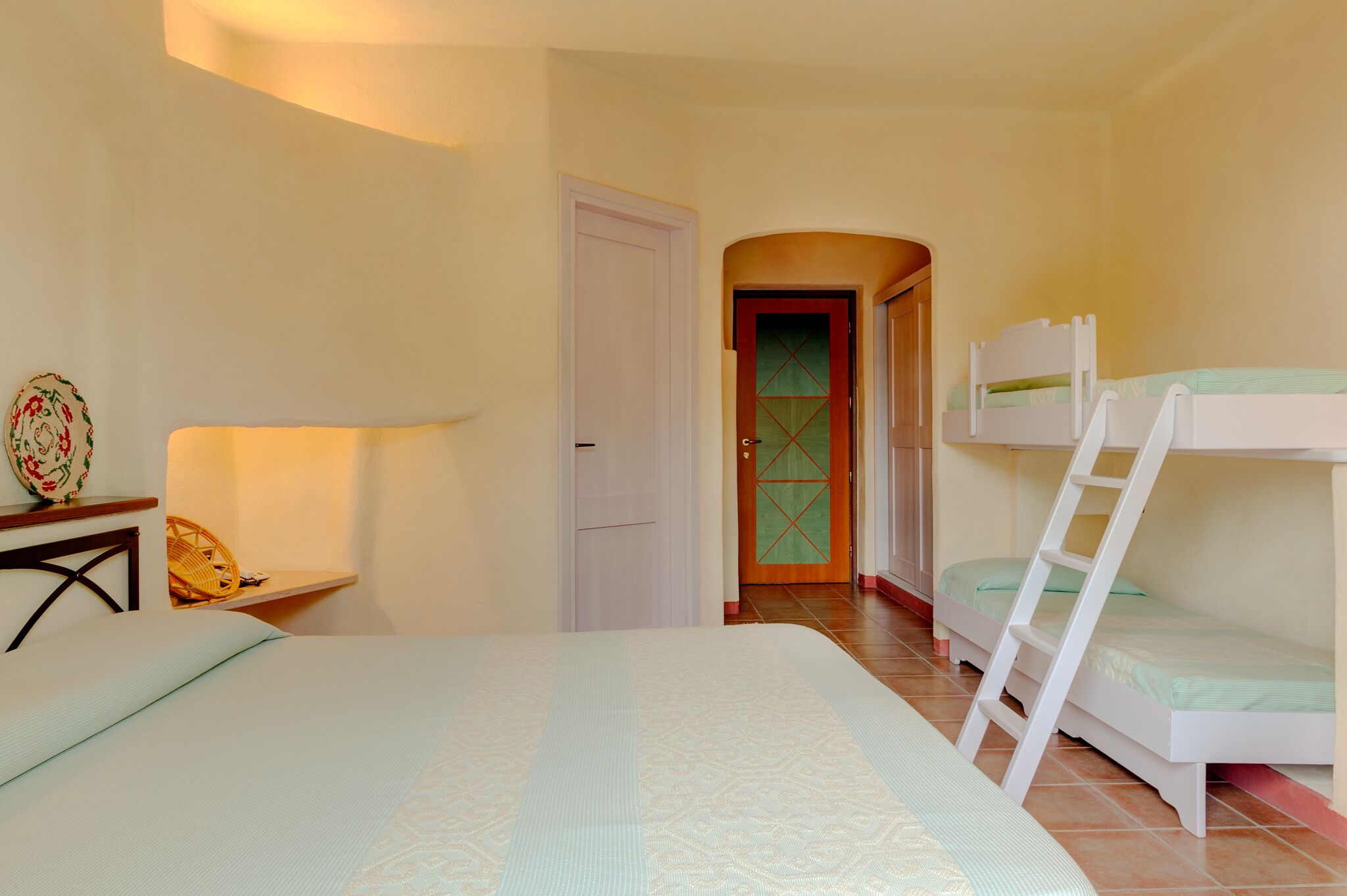 Une chambre avec un lit simple, un bureau avec une lampe et deux lits superposés.