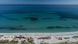 Vista aérea de una zona costera con aguas azules cristalinas, una playa de arena y un pequeño edificio con un muelle.