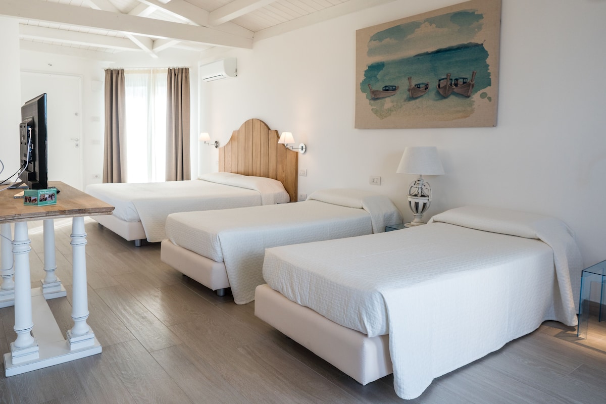 Habitación de hotel con tres camas, un escritorio con computadora, un cuadro en la pared y una ventana con cortinas.