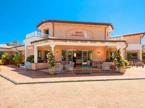 Un hotel con entrada cubierta, mesas al aire libre y plantas en macetas.