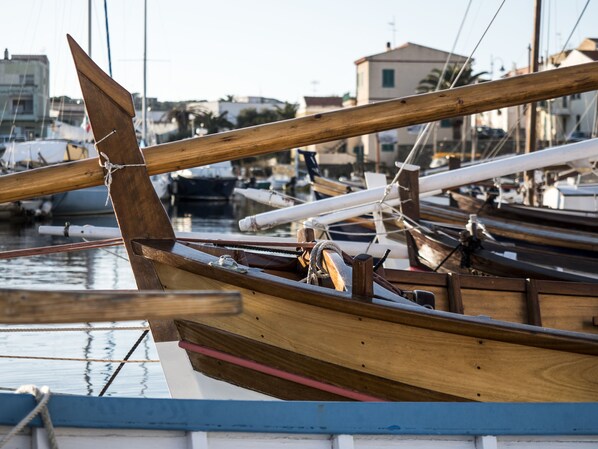 Un bateau en bois, avec une proue en bois et une coque blanche, est amarré dans une marina, parmi d’autres bateaux.
