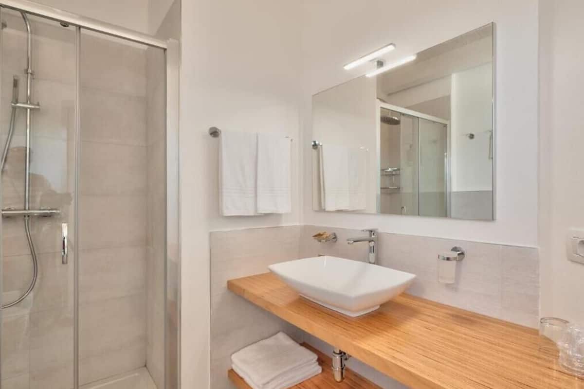 Un baño moderno con cabina de ducha de vidrio, tocador de madera con lavamanos blanco y un espejo grande.