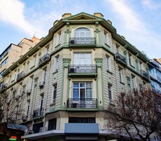 Un edificio en esquina con ventanal tipo mirador, balcones y un cartel de hotel visible.