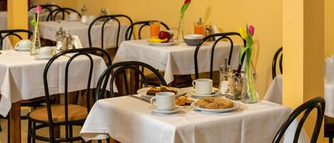 A dining area with tables set for breakfast, including plates of food, cups, and a vase with flowers.