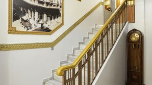 Una escalera con escalones de mármol y barandilla de madera, que conduce a una habitación con una fotografía grande enmarco y un reloj en la pared.