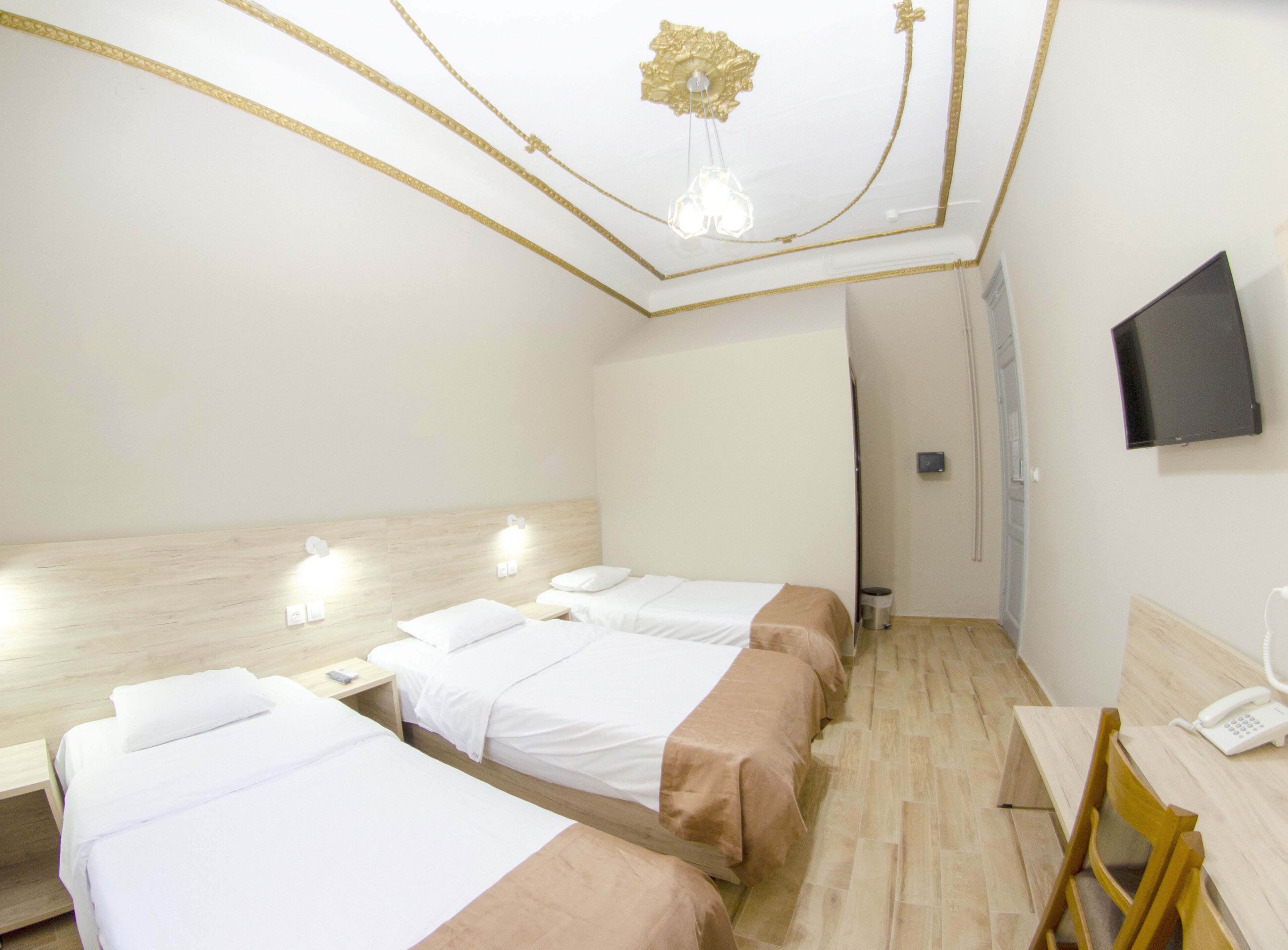 A hotel room with two beds, a desk, a chair, a TV, and a ceiling light fixture.
