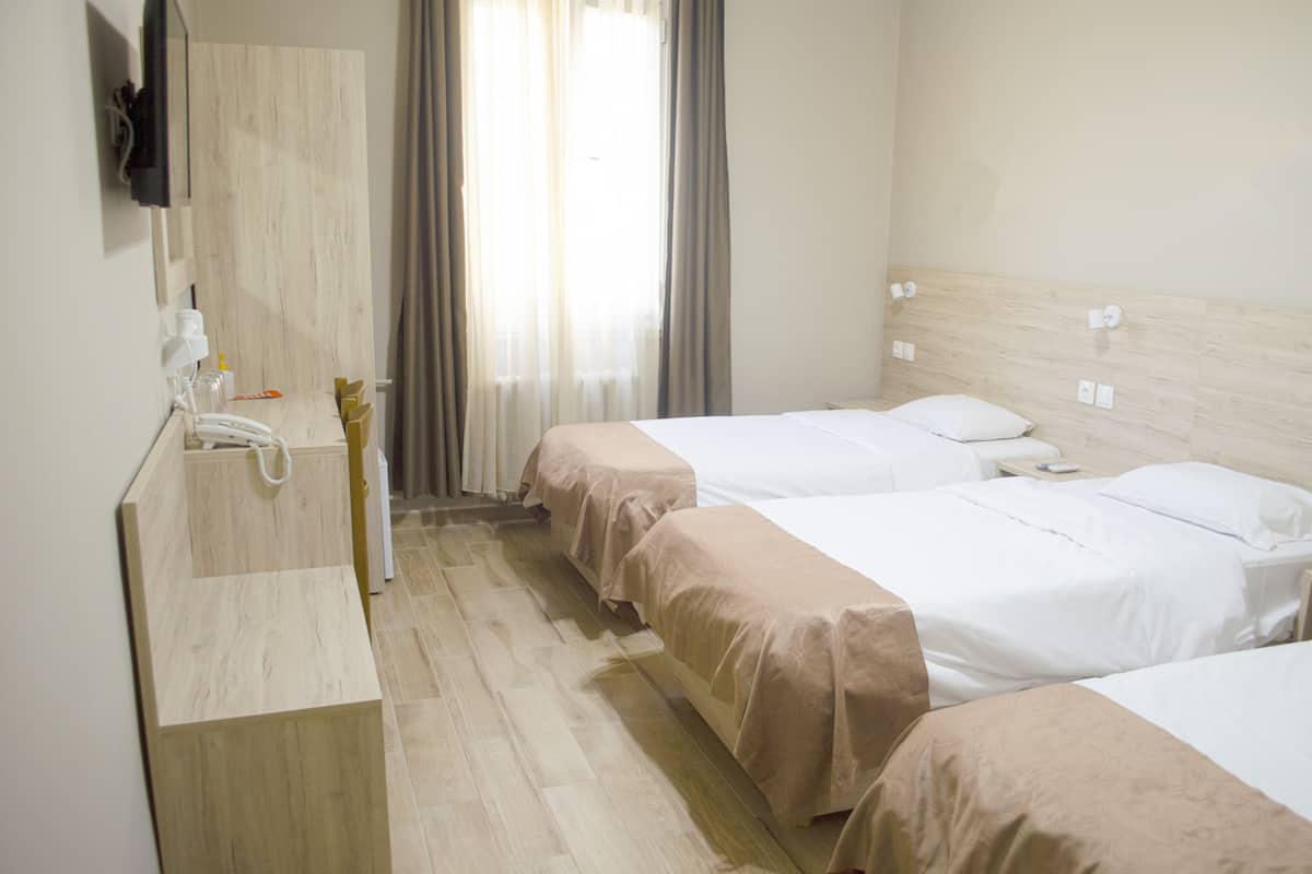Habitación de hotel con dos camas, cabecera de madera, un espejo, un lavamanos y una ventana con cortinas.