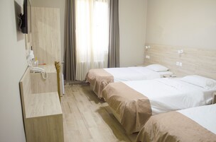 Habitación de hotel con dos camas, cabecera de madera, un espejo, un lavamanos y una ventana con cortinas.