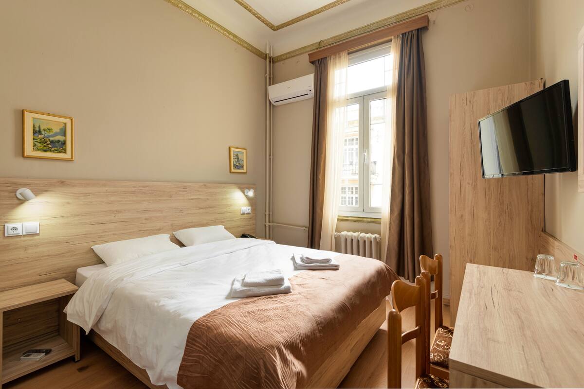 Habitación de hotel con cama, mesita de noche, escritorio con sillas, televisor y aire acondicionado.