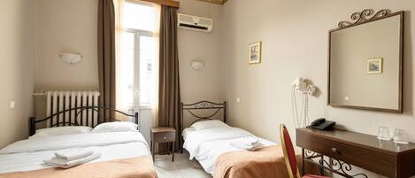 Habitación de hotel con dos camas, un escritorio, una silla, un aire acondicionado, un radiador y una ventana con cortinas.