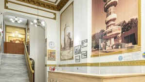 Zona de recepción con un mostrador de madera, una escalera y una pared decorada con cuadros y un cartel grande de una torre.