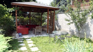 A covered outdoor seating area with a wooden pergola, a red sofa, and a small table with chairs. - B&B Hotel Bicocca (Milan)