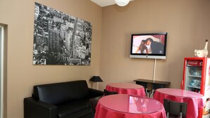 A room with a black leather sofa, two round tables with red tablecloths, a television on the wall, and a Coca-Cola refrigerator. - B&B Hotel Bicocca (Milan)