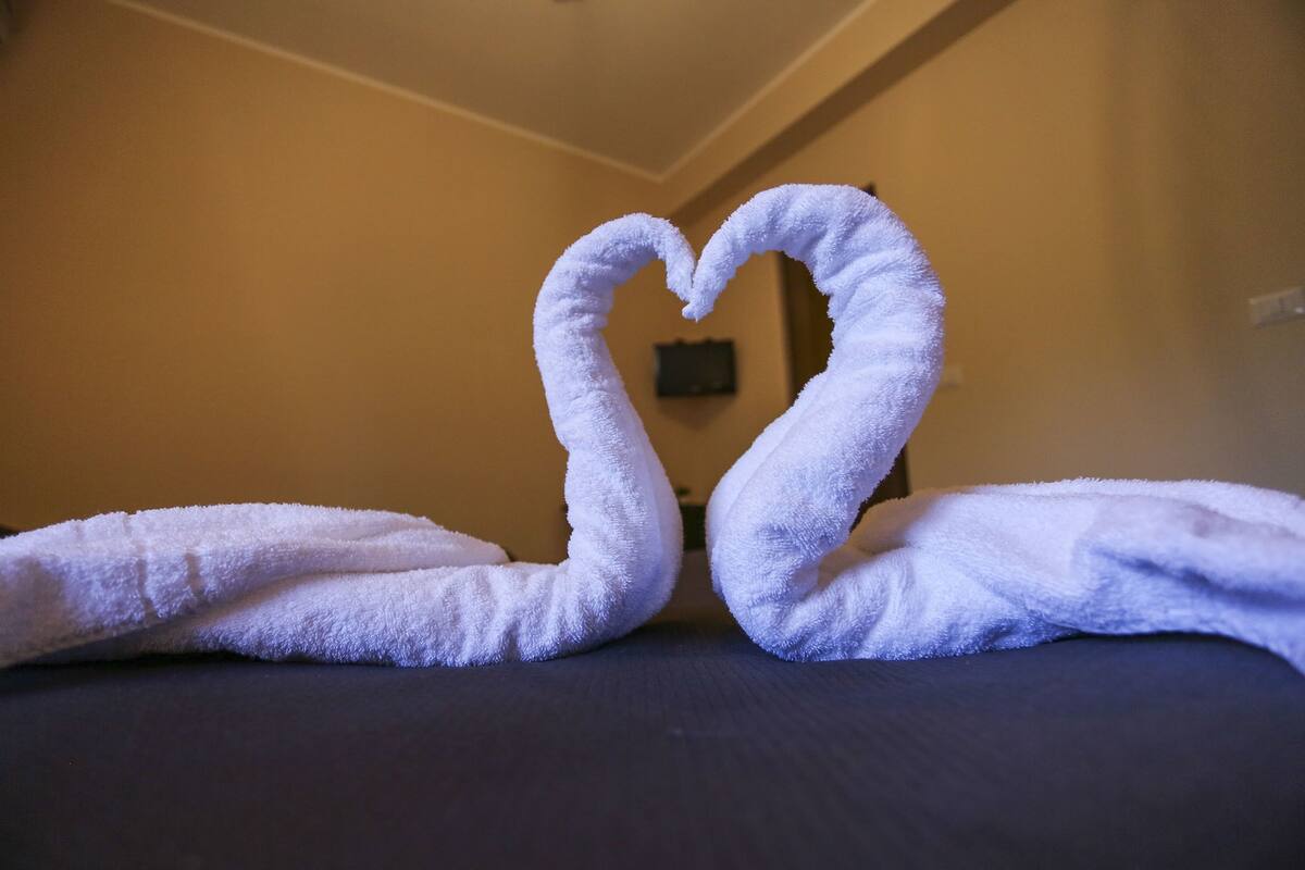 A bed with two towels arranged in a heart shape.