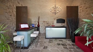 Una habitación con paredes de piedra, una zona de bar, taburetes de bar, un sofá rojo y un candelabro.