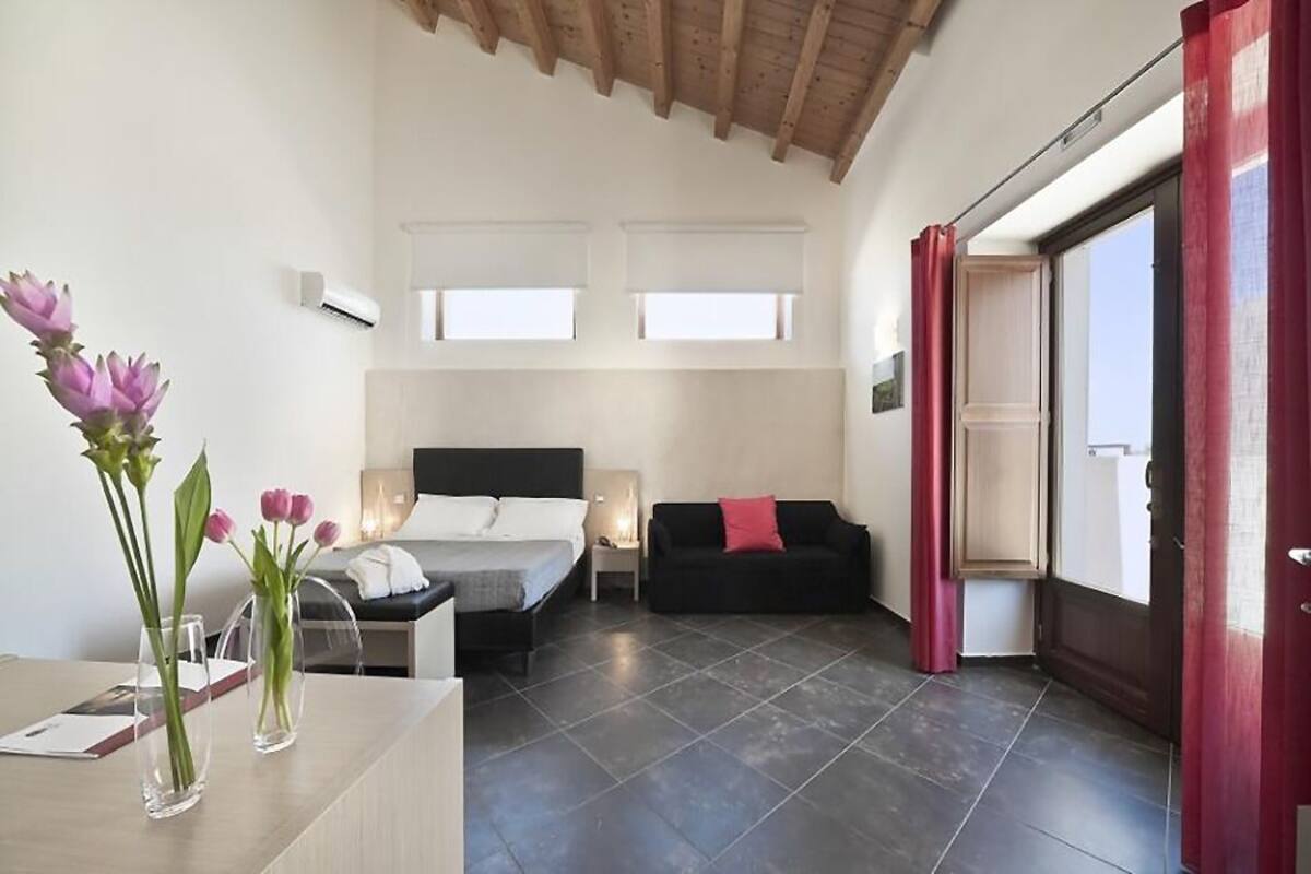 Un dormitorio con cama, mesitas de noche, un sofá negro y una ventana.