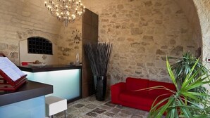 Habitación de paredes de piedra con un sofá rojo, una araña y un mostrador de recepción.