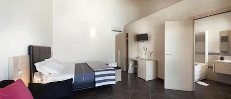 Un dormitorio moderno con cama, mesita de noche y escritorio con silla. Cuenta con un baño con inodoro, lavabo y espejo.