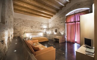 Un dormitorio con paredes de piedra, techo de madera, cama, escritorio y televisor.